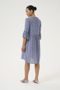 Abito blu a fantasia con maniche a volant e vita arricciata. Collo rotondo. Indossato con tacchi blu slingback; tessuto morbido.