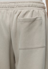 Gros plan sur un pantalon de survêtement beige clair avec une ceinture élastique et une grande poche carrée sur le côté.