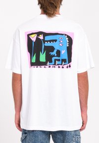 Wit oversized t-shirt met een kleurrijk grafisch ontwerp op de achterkant, met een blauwe creatuur, groene elementen en roze accenten.