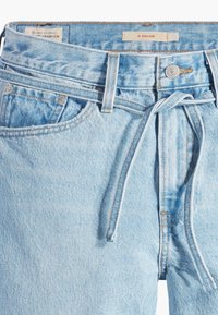 Ljusblå denimballongjeans med hög midja, dragsko, framfickor och kopparnitdetaljer. Slät struktur, avslappnad design.