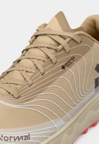 Šviesiai rudas bėgimo batelis, turintis tekstūruotą paviršių, kontrastines baltas bangas ir Gore-Tex logotipą. Šnerves tvirtai pritvirtintos.