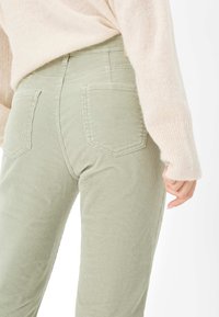 Lys grønne kordfløjspants med en struktureret overflade, høj talje og to baglommer, parret med en blød beige sweater.