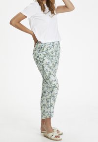 Bílý tričko s textem, spárované s květinovými kalhotami v zelených a modrých odstínech, které mají volný střih a boční lemování.