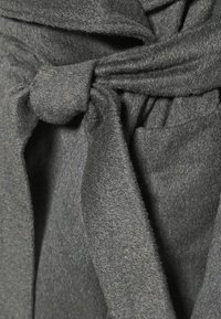 Szary, miękki, teksturowany materiał z wiązaniem w talii i luźnymi fałdami, prezentujący delikatny spływ i minimalistyczne elementy wzornictwa.