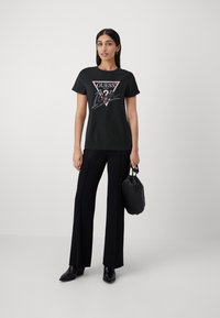 Sort bomuld t-shirt med et grafisk print af et trekantet logo med metallic accenter. Kombineret med sorte brede bukser og ankelstøvler.