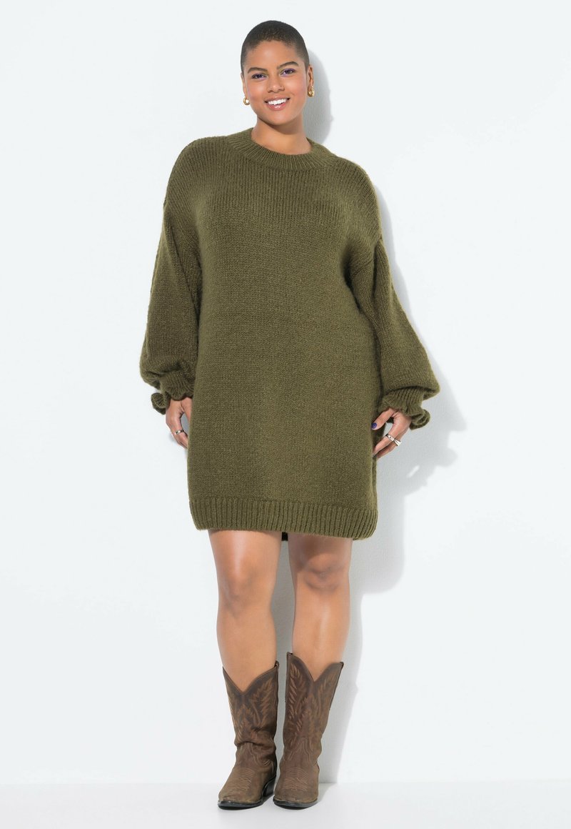 Olivgrünes gestricktes Kleid mit lockeren Ärmeln und geripptem Saum. Kombiniert mit braunen Cowboy-Stiefeln mit strukturiertem Design.