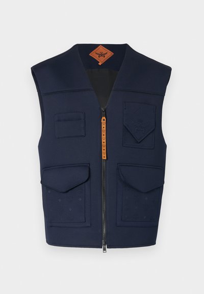 Gilet marine avec fermeture éclair à l'avant, plusieurs poches et un motif en relief. Il présente une texture matelassée et une étiquette en cuir marron.