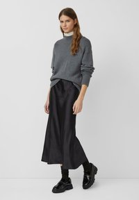 Grijze gebreide trui met een hoge kraag, gecombineerd met een lange zwarte rok. Zwarte chunky schoenen maken de outfit compleet. Soepele texturen en modern ontwerp.