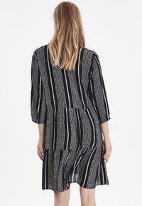 Mustavalkoinen raidallinen mekko, jossa on 3/4-hihat, kerroksellinen helma ja tekstuurinen kangasmalli. Mekko on löysästi istuva ja keskikokoinen.