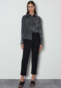 Grijze satijnen overhemd met lange mouwen, gecombineerd met hoge zwarte broeken en zwarte instapsandalen. Minimalistisch ontwerp en pasvorm.