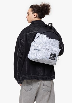 Backpack in black and white with graphic illustrations. Features padded straps, a top handle, and a front pocket. Textured fabric finish.