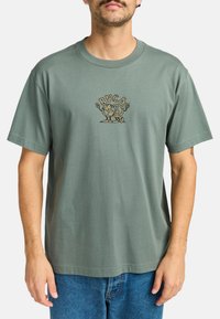 T-shirt in cotone verde con scollatura rotonda, maniche corte e logo grafico a stampa leopardata sul petto. Vestibilità casual.