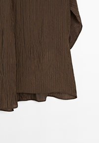 Brunstribet bluse i et blødt, let materiale. Har lange ærmer og en buet kant. Struktureret, plisseret design som tilføjer dybde.