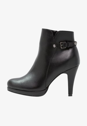 Bottine en cuir noir avec un bout pointu, un talon haut, détail de boucle sur le côté et des accents métalliques, avec une texture lisse.