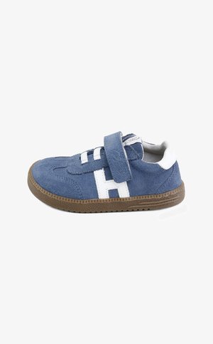 Zapatilla infantil azul de ante con detalles blancos, velcro y suela de goma marrón texturizada, fotografiada sobre fondo blanco.