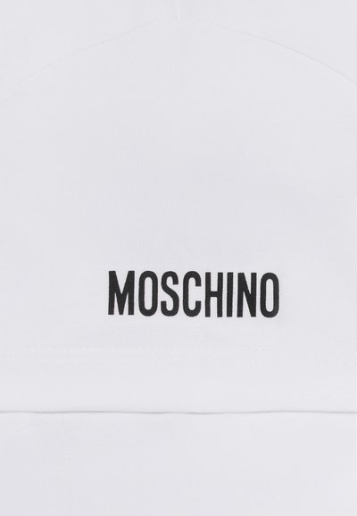 Vitt bomullstyg med en framträdande svart "MOSCHINO"-logotyp. Tyget har en slät yta och en ren, minimalistisk design.