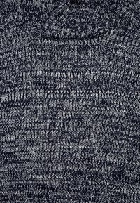 Tissu tricoté bleu marine avec un motif texturé parsemé de petites touches de gris clair, créant un contraste subtil dans tout le matériau.