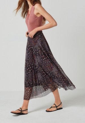 Lyserød ribbet ærmeløs top parret med en lang, flydende sort nederdel med farverige blomster mønstre. Sorte flade sandaler med nitter.