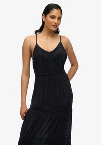 Czarna sukienka bez rękawów z cienkimi ramiączkami, teksturowana góra z koronkowymi detalami, warstwowa spódnica oraz luźny krój.