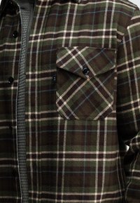 Geruite flanellen blouse in groen, bruin en roomkleur met een borstzak, zwarte knopen en een getextureerde binnenlaag.