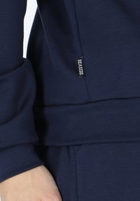Navy sweatshirt with a soft texture and fitted cuffs, featuring a stitched brand tag labeled "SEASIDE" on the side seam.