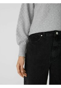 Lichtgrijs, gebreid sweater met textuur en pofmouwen, gedragen met hoge zwarte denim jeans, met knopen en zakken.