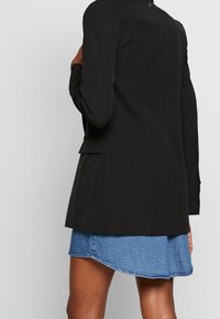 Blazer negro con diseño entallado, mangas largas y bolsillos laterales, combinado con una falda de mezclilla. Tejido suave con una silueta estructurada.