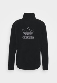 Svart fleecetröja med hög krage, med en vit broderad Adidas-logotyp och bladdesign på baksidan. Långa ärmar med muddade ändar.