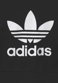 Svart bomullströja med en vit Adidas-logotyp, som består av tre bladliknande former ovanför tre horisontella ränder och fetstilad text nedanför.