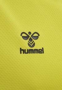 Zwart "hummel" bijenlogo en tekst op een gestructureerde felgele stoffen achtergrond, waarschijnlijk sportkledingmateriaal.