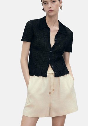Chemise noire à manches courtes avec un motif texturé, boutonnière à l'avant et ourlet festonné. Associée à un short en beige avec cordon de serrage.