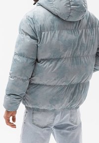 Puffermantel in hellblau mit einer weichen, strukturierten Oberfläche, ausgestattet mit einer Kapuze und elastischen Bündchen, in entspannter Passform mit horizontalen Nähten.