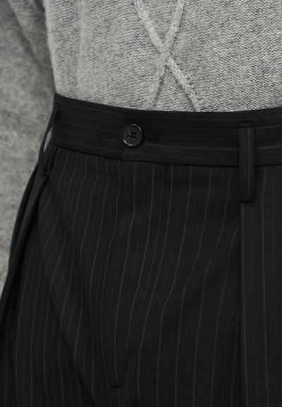 Μαύρο παντελόνι με ρίγες και κουμπωτό κλείσιμο, με ίσια μπροστινή όψη και πιέτες. Η ζώνη διαθέτει θηλιές για προσαρμοσμένη εφαρμογή.