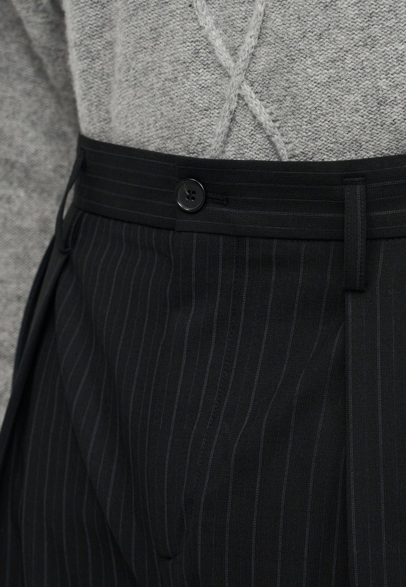 Black pinstriped trousers with a button closure, featuring a flat front and pleats. The waistband has belt loops for adjustable fit.