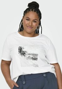 Valkoinen puuvillapaita, jossa on mustavalkoinen painettu ranta-aiheinen kuvasto, koristeltuna koristehelmillä kuvan ympärillä. Pyöreä pääntie, lyhyet hihat.