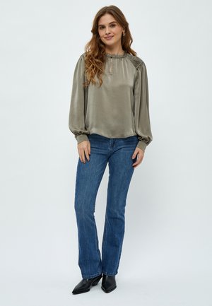 Satin olivengrøn bluse med lange puffærmer, indsamlet halsudskæring, nøglehulldetalje, parret med blå flagrende jeans og sorte hælhøje støvler.