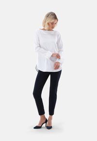 Blusa bianca a maniche lunghe con scollatura ampia, abbinata a pantaloni aderenti blu navy e tacchi alti in suede neri. Tessuto liscio con un design classico.