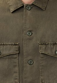 Olivgrünes Hemd mit Knöpfen aus strukturiertem Stoff, mit zwei Fronttaschen und runden Kunststoffknöpfen.