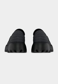 Chaussures noires sans lacets avec une tige en tissu texturé, des détails nervurés, et une semelle épaisse dentelée pour une meilleure adhérence.