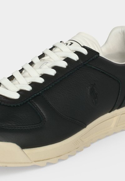 Μαύρα δερμάτινα αθλητικά παπούτσια με λευκά κορδόνια, μπεζ σόλα και ανάγλυφο λογότυπο στο πλάι, εμφανίζοντας λεπτομέρειες πλαγίως και από πάνω.