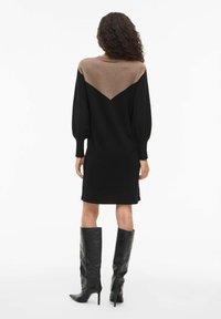 Abito nero in maglia con maniche lunghe, caratterizzato da un motivo triangolare marrone sul retro, abbinato a stivali neri con tacco alto.