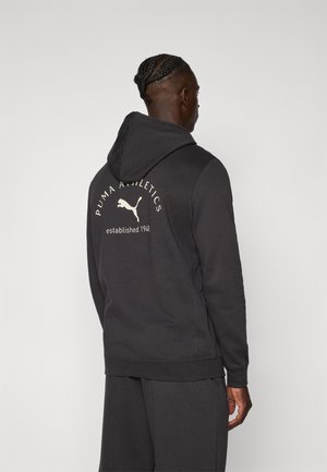 Hooded sweatshirt made of dark fabric, featuring a printed logo on the back. It has a relaxed fit and ribbed cuffs and hem.
