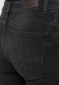 Jeans din denim negru, cu talie medie, având un singur buzunar posterior cu o curbură subtilă, patch din piele cu logo pe talie și țesătură texturată.