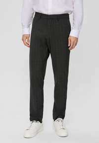 Pantalon gris à motifs avec un design à carreaux, fabriqué en tissu tissé, associé à des baskets blanches. Coupe ajustée avec des coutures repassées.