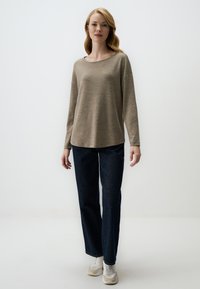 Beige Langarmoberteil mit weitem Ausschnitt, kombiniert mit dunkelblauen geraden Jeans und weißen Sneakers. Glattes Material und lockere Passform.