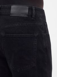 Gros plan sur la poche arrière et la ceinture d'un jean en denim noir avec une étiquette de marque en cuir noir cousue au-dessus de la poche.