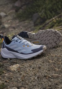 Ζευγάρι μπλε και μαύρα παπούτσια Adidas Terrex για trail running σε βραχώδες έδαφος, που δείχνουν την υφή στην σόλα από καουτσούκ Continental.