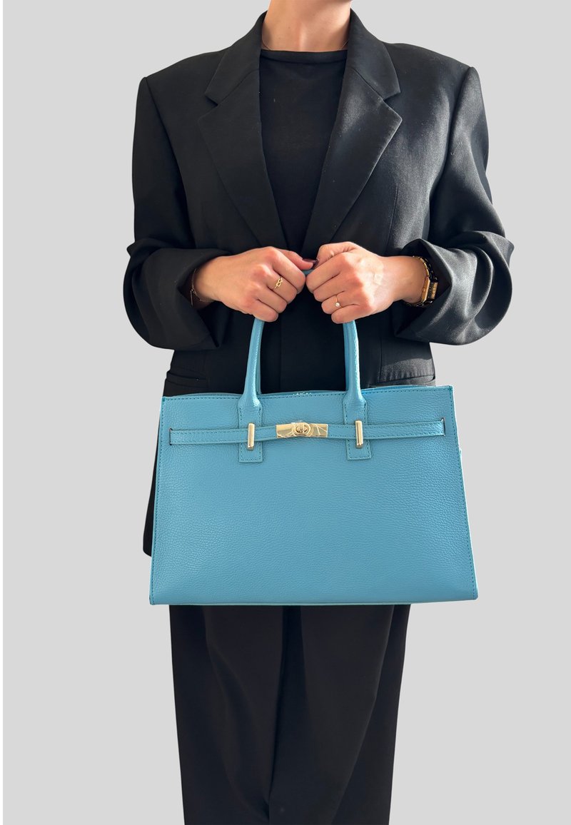 Niebieska skórzana torebka o strukturalnym kształcie, z górnymi uchwytami i srebrnymi akcentami metalowymi. Powierzchnia ma gładką teksturę i minimalne detale.