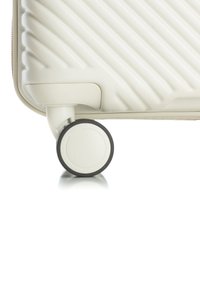 Witte harde koffer met horizontale ribbels en een zwarte rubberen wieltje. Het wieltje heeft een witte kern en is bevestigd aan een gladde basis.