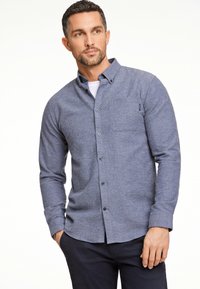 Overhemd met knopen in een gemêleerde blauwe stof. Heeft een borstzak, lange mouwen en een afgeronde zoom. Gemaakt in combinatie met donkere broeken.